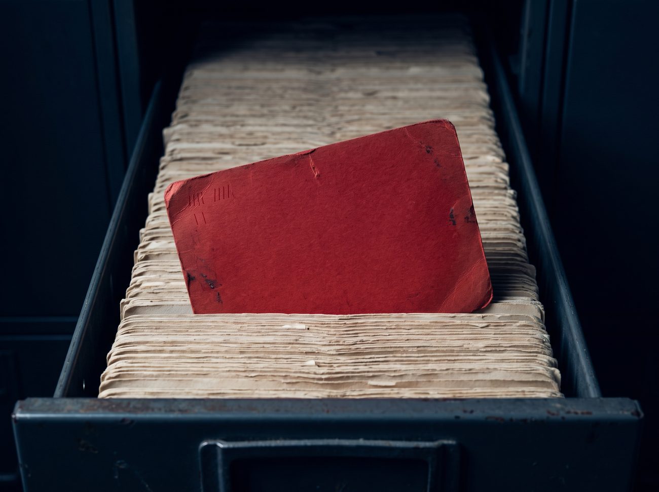A single aged red index card pulled forward from a drawer of hundreds of identical cards